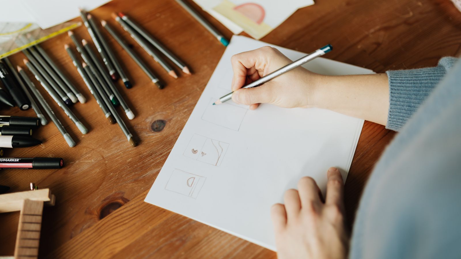 Designer qui esquisse des pistes de logo au crayon sur une feuille, entourée de feutres